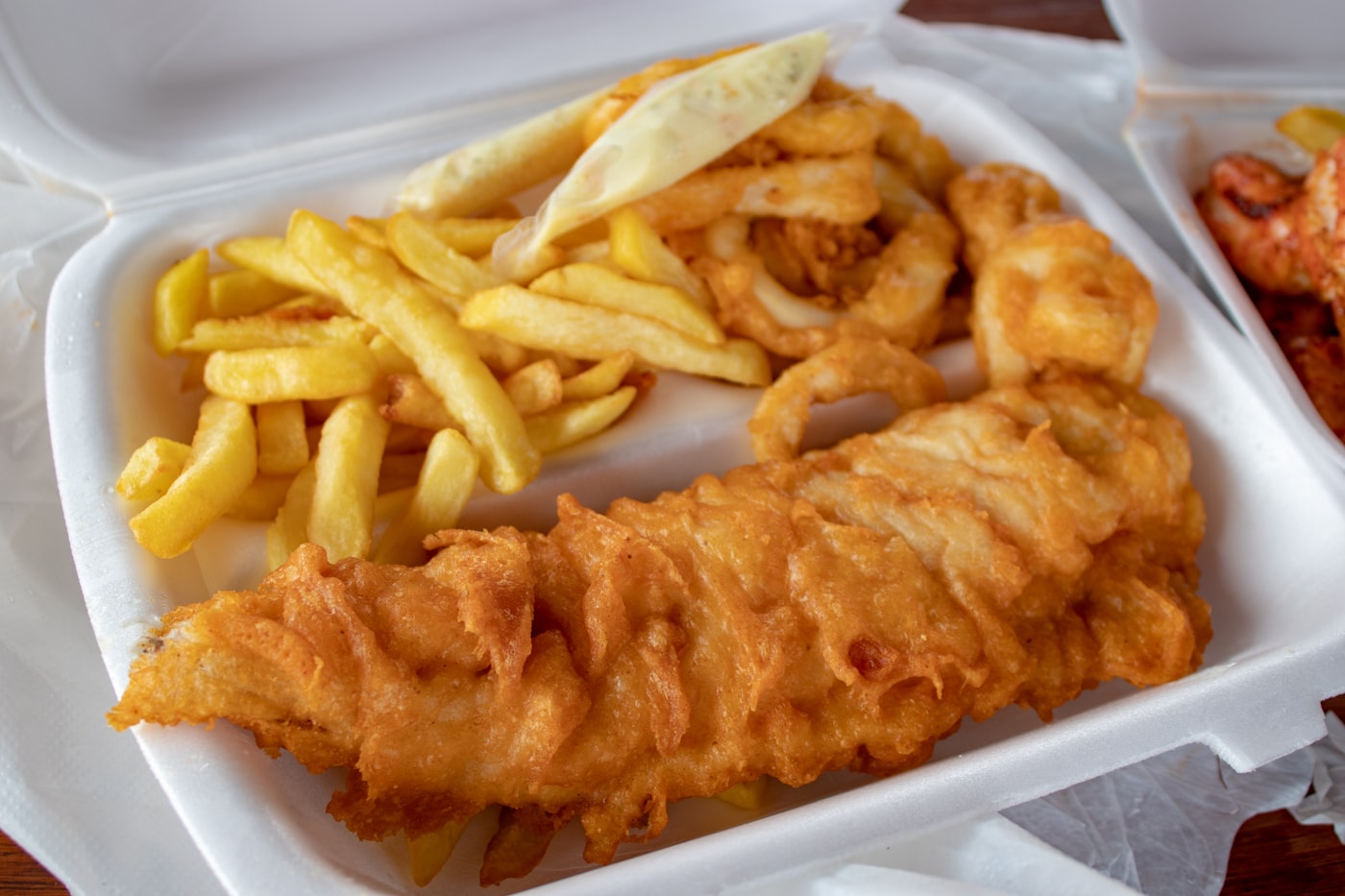 A fried fish fillet in a foam carry-out box with chips and a tub of tartar sauce.